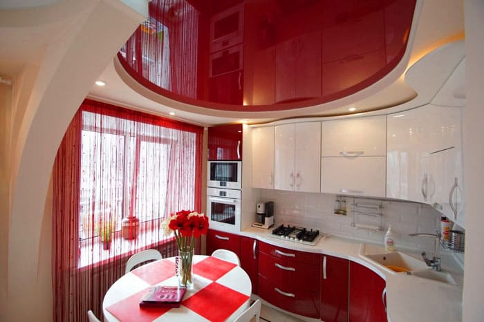 Червеният и бял интериор на кухнята изглежда интересно поради дизайна на самата слушалка и повторението на нейната геометрична форма на тавана
